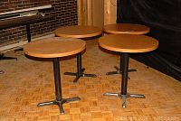 Four round bistro tables arranged upright with wood grain tops and black metal bases on a parquet floor.