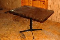 Full view of the rectangular table showing the dark melamine and plywood top with visible wear and metal base with four legs.