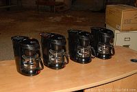 Four Sunbeam 4-cup coffee makers on table, black with glass carafes and red indicator lights.