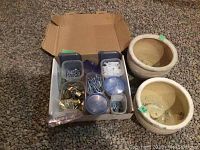 Photo of assorted hardware items in plastic containers including screws, anchors, small brass padlocks, and keys in a cardboard box alongside two ceramic garden pots
