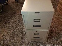 Front view of the filing cabinet showing two drawers with label slots and handles on a gravel surface.