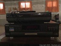 View of the front side of the two stacked units on a dark surface, showing Technics CD changer below and Hitachi VHS player above.