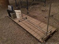 Full view of metal clothing rack frame laid on the ground, showing base with horizontal metal rods and attached wheels.
