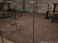 Full view of the metal clothes rack standing on a gravel surface, showing the horizontal hanging bar and base structure.