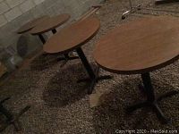 Four round restaurant style bistro tables shown in a row outdoors on gravel surface, showing tops and bases.