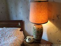 Vintage ceramic base lamp with floral design and fabric shade on, near bed.
