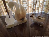 Two onyx decorative figures on a piano with background window and curtains. One piece is a pair of swans on an onyx base, the other is an abstract bird figure.