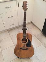 Full front view of the natural wood acoustic guitar showing body, sound hole with black pickguard, fretboard, and headstock.