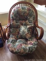 Front view of rattan papasan chair showing the tropical leaf cushioned seat with matching pillow and curved rattan frame.