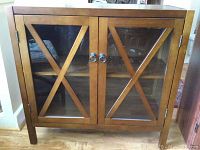 Front view of the wooden cabinet showing two glass panel doors with X-shaped wooden braces and metal ring handles.