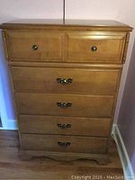 Front view of wooden dresser showing five drawers: two small top drawers with round metal knob handles, three larger bottom drawers with decorative pull handles.