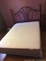 Full view of assembled double bed with white mattress and black metal headboard against purple wall