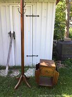 Full view of wooden coat tree and vintage wood tobacco side table set outside with metal shed background