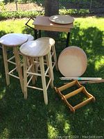 View of stools, two round wooden table tops, wooden spice rack laid on grass showing natural wood finish.
