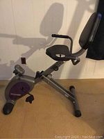 Side view of the full stationary bike with seat and backrest visible, showing the gray and purple color scheme.
