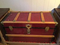 Photo showing front and top view of red storage chest with wood reinforcements and brass hardware.