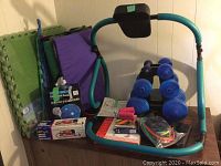 Photo showing ab cruncher frame, blue hand weights, foam mats, and various exercise accessories.