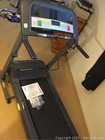 Treadmill overview showing the frame, running belt, handles, and instruction manual on the belt.