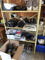Wide shot showing shelves holding scanner/printer, speakers, PC tower, power adapters, and other electronics in boxes