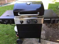Front view of entire grill outdoors showing main body, control panel, side shelves, wheels and propane tank holder