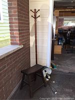 Side view of wooden coat tree, bench, and wall lamp placed against brick and siding walls