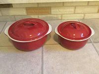 Two red covered stoneware casserole bowls side-by-side, viewed from top angle showing lids.