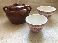 Brown ceramic bean pot with lid and two ceramic bowls with England style red transferware pattern on kitchen counter.