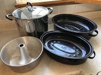 Photo showing stainless steel stockpot with lid and two black enamel-coated roasting pans with leaf design.