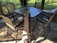 View of square glass top table with four metal frame folding chairs on outdoor patio