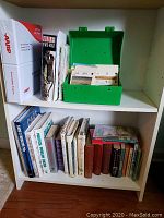 Bookshelf with arranged hardback and paperback books, a green wildlife card catalog box with cards inside, and an AARP driver safety manual binder.
