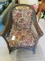 Front view of wicker rocking chair with floral cushions showing wear on arms.