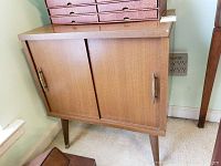 Mid-century wooden record cabinet with sliding doors and metal handles on tapered legs