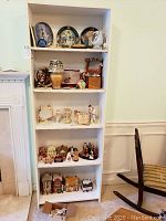 Full view of bookshelf with four shelves holding Christmas collectible plates, nativity sets, ornaments, and miniature houses.