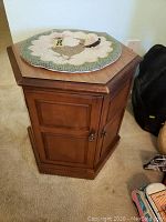 Photo of the smaller pressed wood octagonal end table with cabinet door, lock latch, and octagonal top with decorative mat.