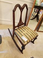 Front angle showing the carved wooden backrest and the worn striped fabric seat upholstery on the rocking chair.
