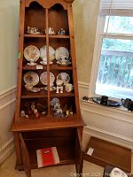 Wood glass-front cabinet with plates, miniature tea sets and collectibles arranged on four shelves.