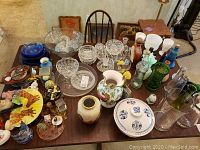 Top view of glassware including milk glass, hobnail, crystal cut glass, blue and green glass pieces, vases, decanters, and decorative figurines on a table.