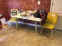 Kitchen table and two yellow chairs set with various items on table (not included). Shows full setup and general condition.
