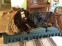 Seven coats and jackets, including vintage faux fur coats and men's brown leather jackets with caps, spread out on green couch.