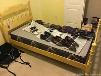 Full view of yellow painted solid wood bed frame with mattress showing items placed on mattress bed frame is making up. Room background shows plugged wall outlet and other furniture