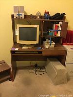 Full view of wood desk with computer monitor, keyboard shelf pulled out, and items on desk. Rolling stand partially visible at left. File cabinet on right side.