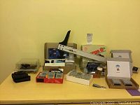 Photo showing assortment of tools, batteries, razor blades, T-square, knives, and office supplies arranged on table