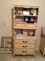 Full view of cream dresser and hutch with assorted collectibles, framed art, and clocks displayed
