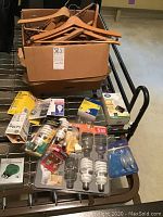 Box filled with wooden hangers placed on a cart, with various light bulbs spread in front also on the cart, showing details and packaging.