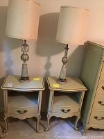 Front view of the two French Provincial style night stands with lamps on top, showing the overall design and shape.