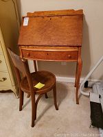 Full view of the maple secretary desk and wooden chair showing the desk's slant front and drawer and the chair positioned in front of the desk.