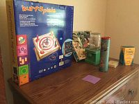 Wurf Spiele ring toss game box, wooden Pick Up Sticks cylindrical container, Crayola crayons box, flash cards and other items on wooden dresser