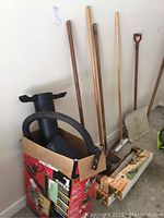 Photo showing two manual lawn edgers with metal blades and wheels, hoe, brush, snow shovel, and box containing Toro blower adapter with hose and tube.