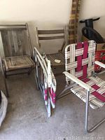 Two vintage wooden folding chairs in natural wood finish and two aluminum folding chairs with white and pink webbed fabric, all folded or stacked visible on concrete floor.