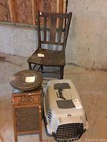 Wide view of the antique chair, metal milk can with lid, wooden washboard, and plastic dog carrier arranged on floor.